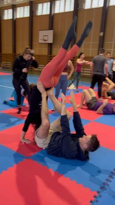 two people doing acrobatic exercises in an indoor gym while others look on