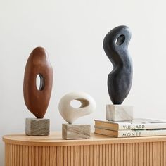 three different sculptures sitting on top of a wooden table next to books and a book