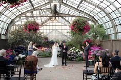 a bride and groom standing at the end of their wedding ceremony in a glass walled greenhouse