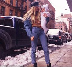 a woman holding a baby in her arms while walking down the street with snow on the ground