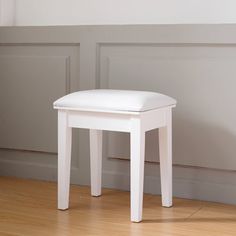 a white stool sitting on top of a hard wood floor next to a wall and window