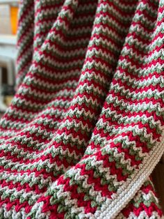 a red and white crocheted blanket sitting on top of a wooden chair next to a window