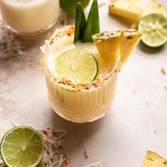 two glasses filled with drinks and garnished with limes, pineapple slices and coconut