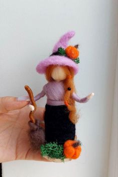 a hand holding a small doll wearing a pink hat and black skirt with an orange nose