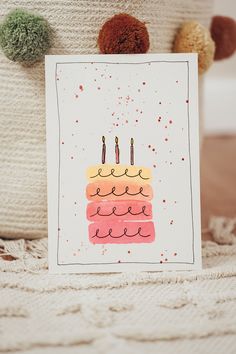 a card with a birthday cake on it next to a teddy bear and pom poms