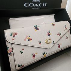 a white coach wallet with flowers on it in a black box next to a card case