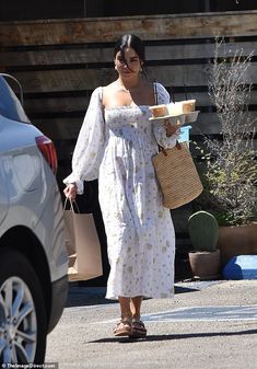 a woman in a white dress is walking down the street holding a basket and shopping bags