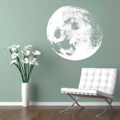 a white chair sitting in front of a green wall with a large moon on it