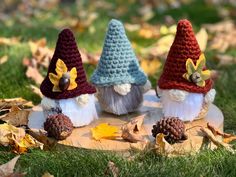 three crocheted gnomes sitting on top of a piece of wood in the grass