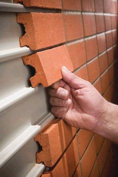 a hand is holding the corner of a red bricked wall and opening it up