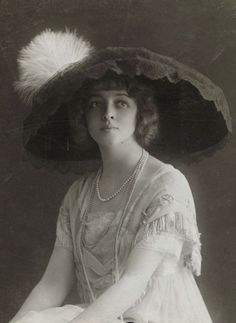 an old fashion photo of a woman wearing a large hat with feathers on the brim