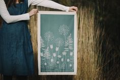 a woman holding up a poster with flowers on it in front of some tall grass