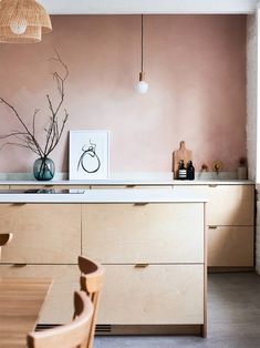 a kitchen with pink walls and wooden furniture in the foreground is a dining table