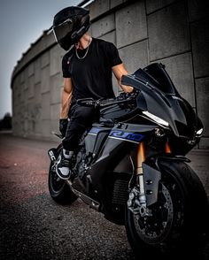 a man sitting on top of a black motorcycle next to a cement wall and wearing a helmet