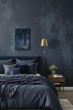 a bed with blue sheets and pillows in a room that has dark walls, wooden flooring and a painting on the wall