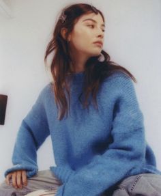 a woman sitting on the floor wearing a blue sweater