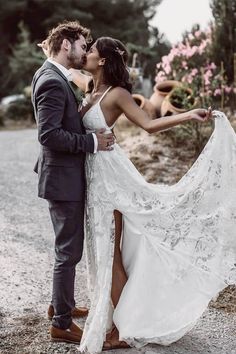 a bride and groom kissing in the middle of a gravel road with pink flowers behind them