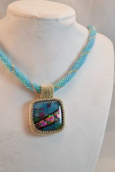 This wonderful hand beaded pendant can be worn with anything, the dichroic glass pendant with shades of purple and turquoise is highlighted with silver color and turquoise beads. Perfect as a gift for yourself, or that special someone, this necklace will come to you in a gift box! Designed and hand beaded by me in my Las Vegas studio, this piece is one of a kind. Pendant measures about 1 1/4 inches tall and across, and the necklace measures approximately 20 inches long. For more of my handmade j Iridescent Beaded Jewelry As A Gift, Iridescent Beaded Jewelry For Gift, Turquoise Beaded Glass Jewelry, Handmade Iridescent Round Bead Jewelry, Handmade Iridescent Jewelry With Round Beads, Blue Beaded Gems And Cabochons For Gift, Iridescent Beaded Necklace For Gift, Handmade Turquoise Glass Beaded Necklaces, Handmade Turquoise Glass Beaded Necklace