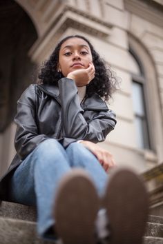 a woman sitting on steps with her hand under her chin looking up at the camera