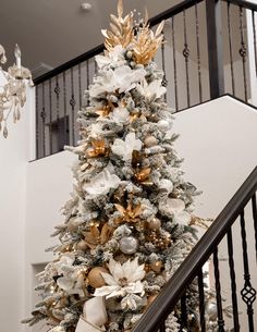 a white christmas tree with gold and silver ornaments on it in front of a banister