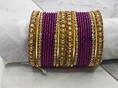 "Purple Shimmer Golden Stones Bangle Set - Beautiful occasion wear jewellery The perfect fusion of tradition and style, designed to elevate your outfit with elegance and charm. This Bangle set is made for two hands and contains 11 pieces in each set. If you want to match the design shown in the picture in single hand, be sure to select a quantity of 2. Notes: Sizes for bangles are Indian sizes so check your exact size as shown in picture before placing and order. Create beautiful memory for any Purple Bangle Jewelry For Wedding, Festive Purple Bangle, Traditional Purple Bracelets For Festivals, Purple Bangle For Wedding, Traditional Purple Bracelets For Festive Occasions, Traditional Adjustable Purple Bangle, Traditional Purple Bangle For Festive Occasions, Traditional Purple Bracelet For Festive Occasions, Festive Traditional Purple Bangle