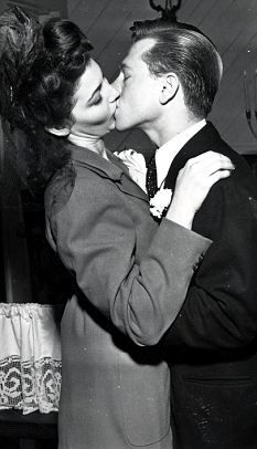 a man and woman kissing in front of a cake