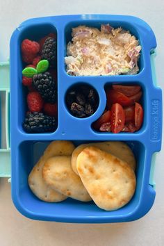 a blue lunch box filled with fruit, crackers and other food items on top of it