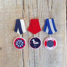 four badges with different designs on them hanging from hooks against a wooden wall, one has a pinwheel and the other is a sailboat