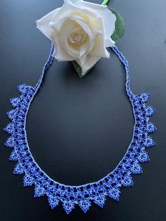 a white rose sitting on top of a blue lace choker with flowers in it