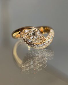 a yellow gold ring with a pear shaped diamond on it's side, sitting on a reflective surface