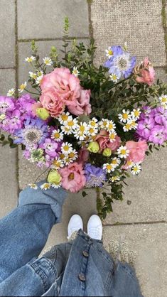 a person's feet are shown next to a bouquet of wildflowers and daisies