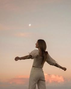 a woman standing on top of a sandy beach next to the ocean with her arms outstretched