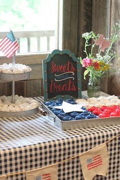 a table topped with lots of desserts next to an american flag sign and potted plant