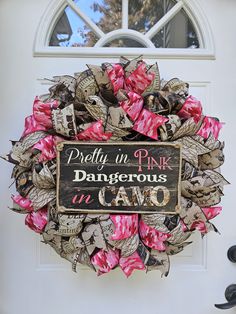 a pink and black wreath is hanging on the front door with a sign that says pretty in pink dangerous to camo