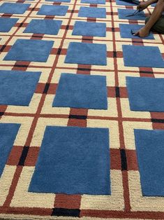 two people sitting on the ground in front of a blue and red rug with squares