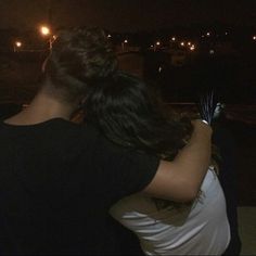 two people standing next to each other with their arms wrapped around one another at night