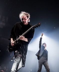 two men playing guitars on stage with one holding his arm up to the other side