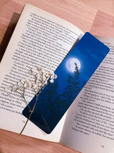 an open book on a table with a flower in the foreground and a full moon in the background