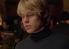 a young man with blonde hair wearing a turtle neck sweater in a bar or restaurant