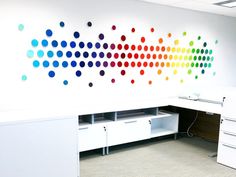 an office cubicle with colorful dots painted on the wall and white desks in front of it