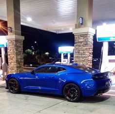 a blue sports car parked in front of a gas station at night with its lights on