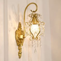 a golden wall light with crystal drops hanging from it's arm and on the wall