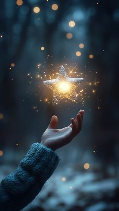 a person's hand holding a glowing star in the night sky with blurry lights