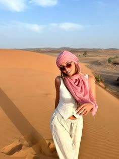 a woman standing in the desert wearing sunglasses and a pink scarf