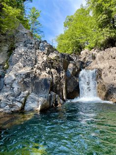 there is a small waterfall in the middle of this body of water with rocks and trees around it