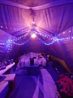 the inside of a tent is lit up with purple lights and blankets on the floor