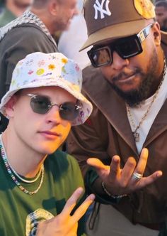 two young men with hats and sunglasses posing for the camera in front of a crowd