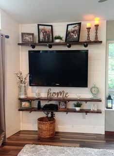 a flat screen tv mounted to the wall above a shelf with pictures and candles on it