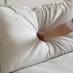 a person holding onto a white pillow on top of a bed