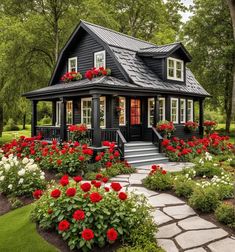 a black house with red flowers in the front yard and steps leading up to it